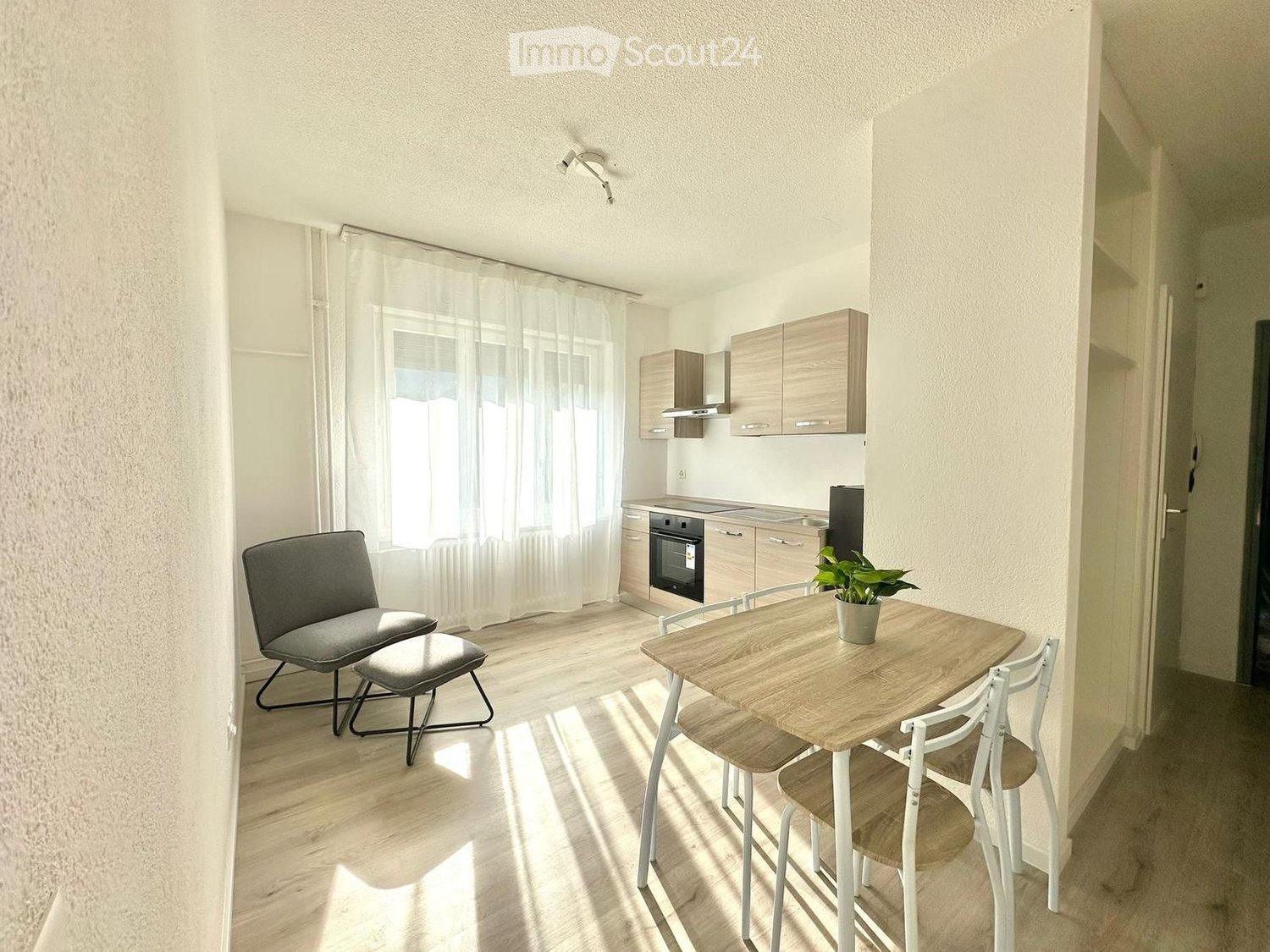modern kitchen with dining area, wooden floor, white walls, white curtains, wooden table, chairs, potted plant, built-in cabinets, oven, microwave, sink, faucet