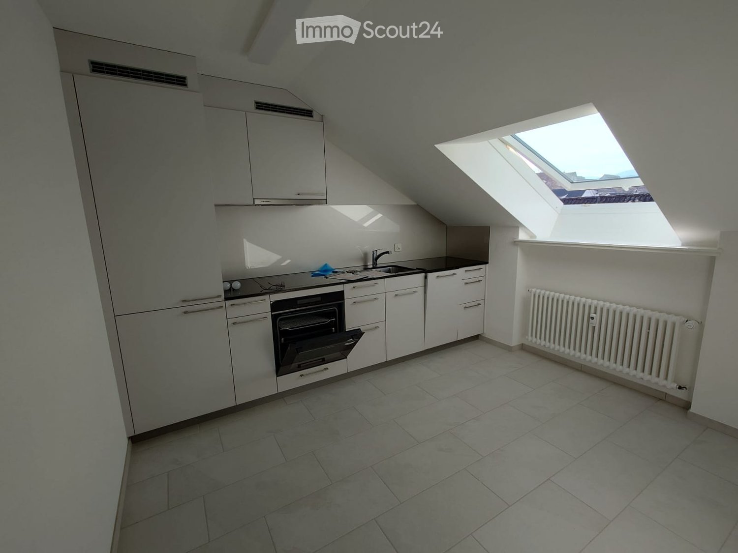 modern kitchen with white cabinets, tiled floor, black countertops, oven, sink, skylight