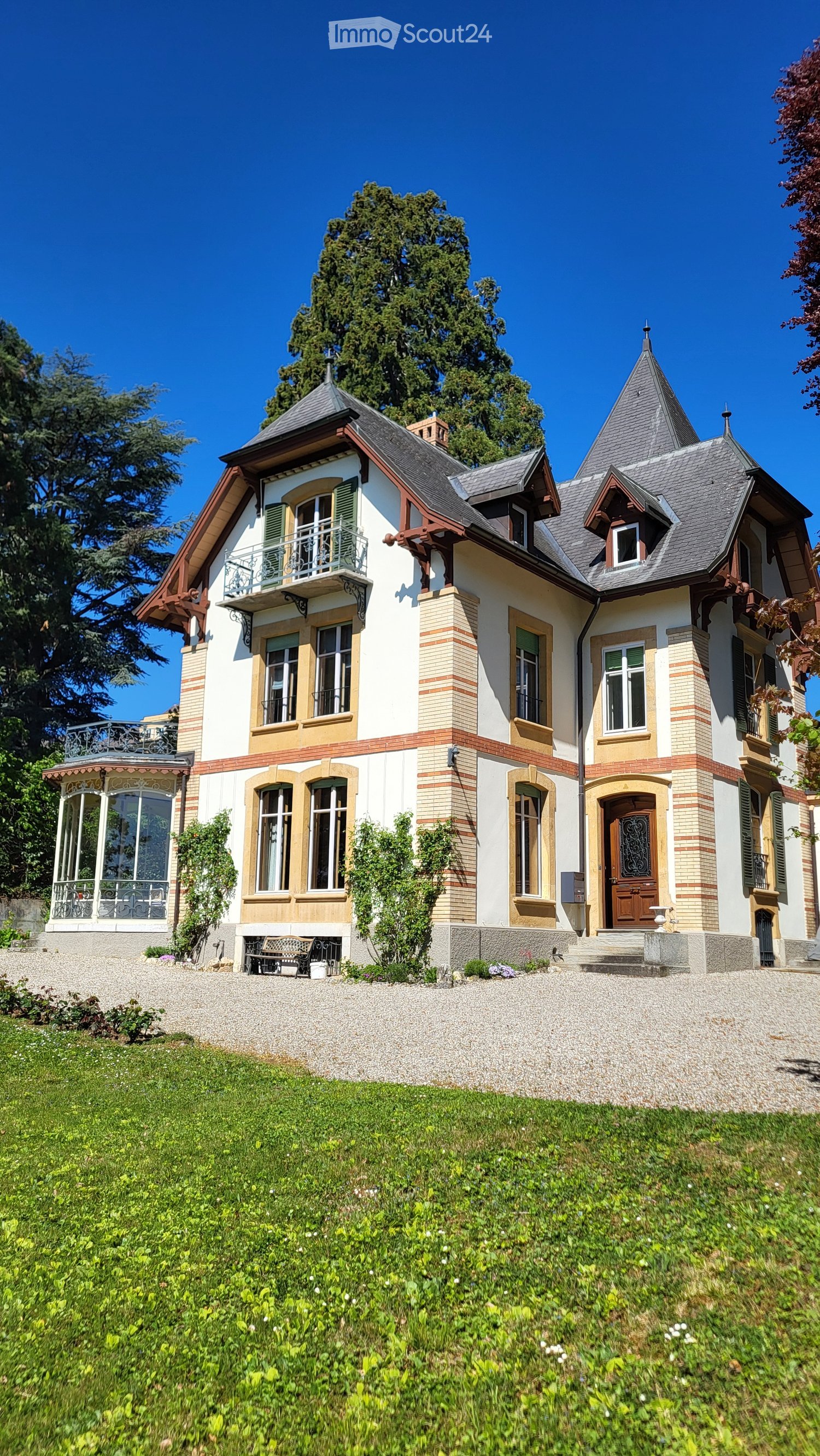 3 story house, white and brown exterior, large windows, balcony, gravel driveway, garden