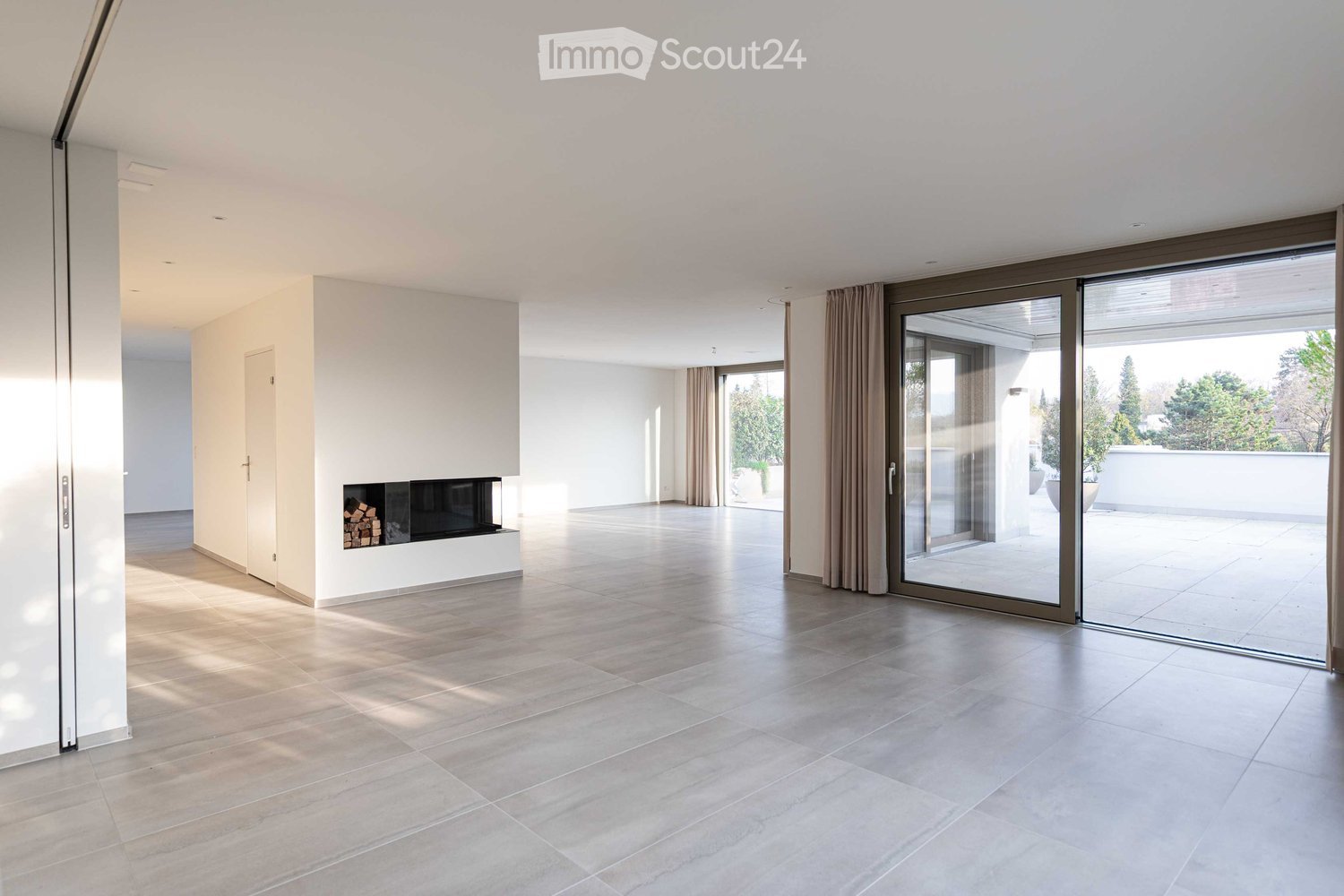 Spacious room with white walls, tiled floor, fireplace, and sliding glass doors.