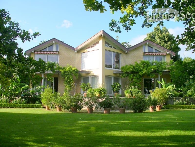 Two-story house with a yellow exterior, large windows, and a well-maintained garden with various potted plants.