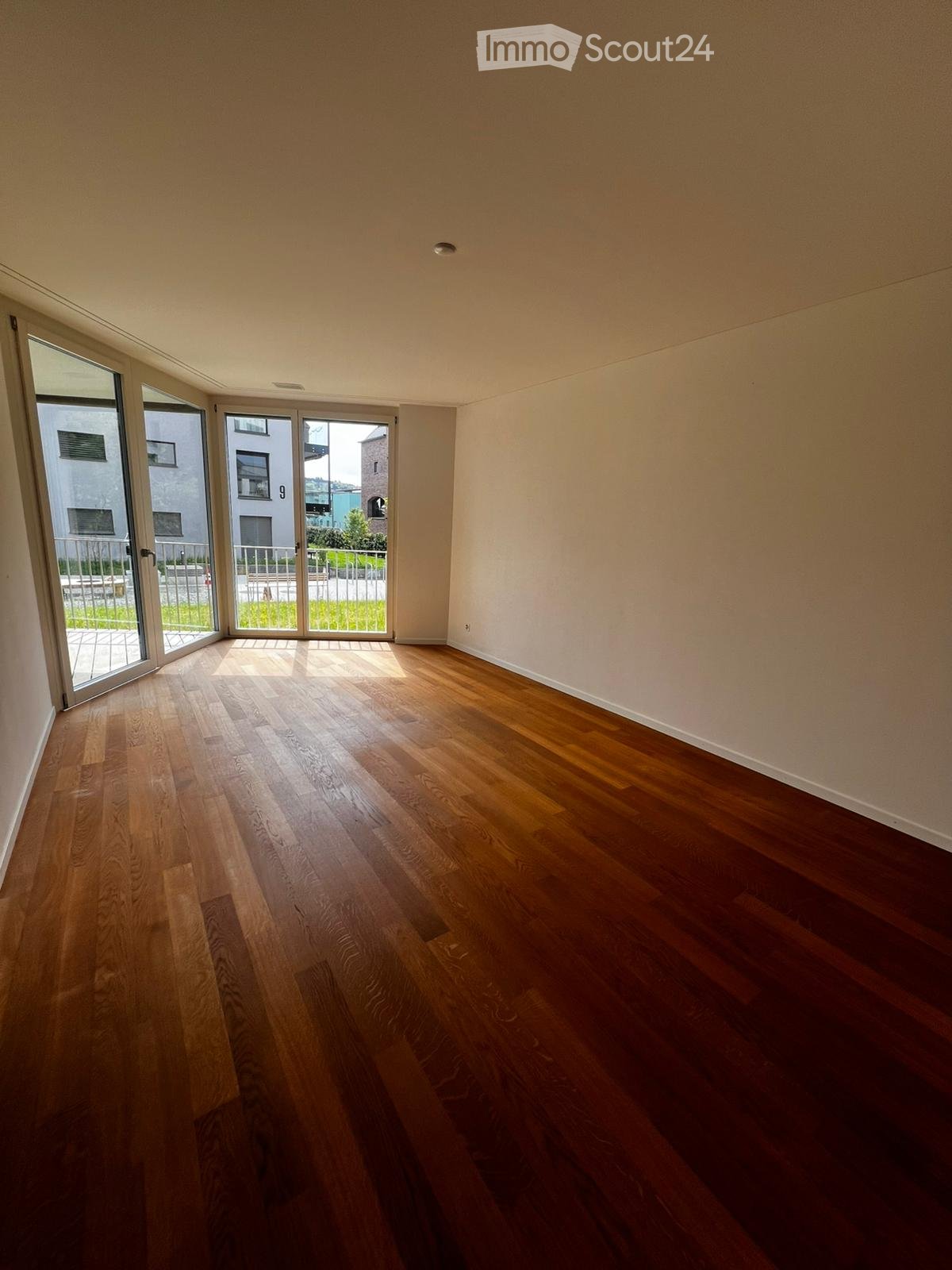 Empty room with hardwood floors, white walls, and large glass doors leading to a balcony.