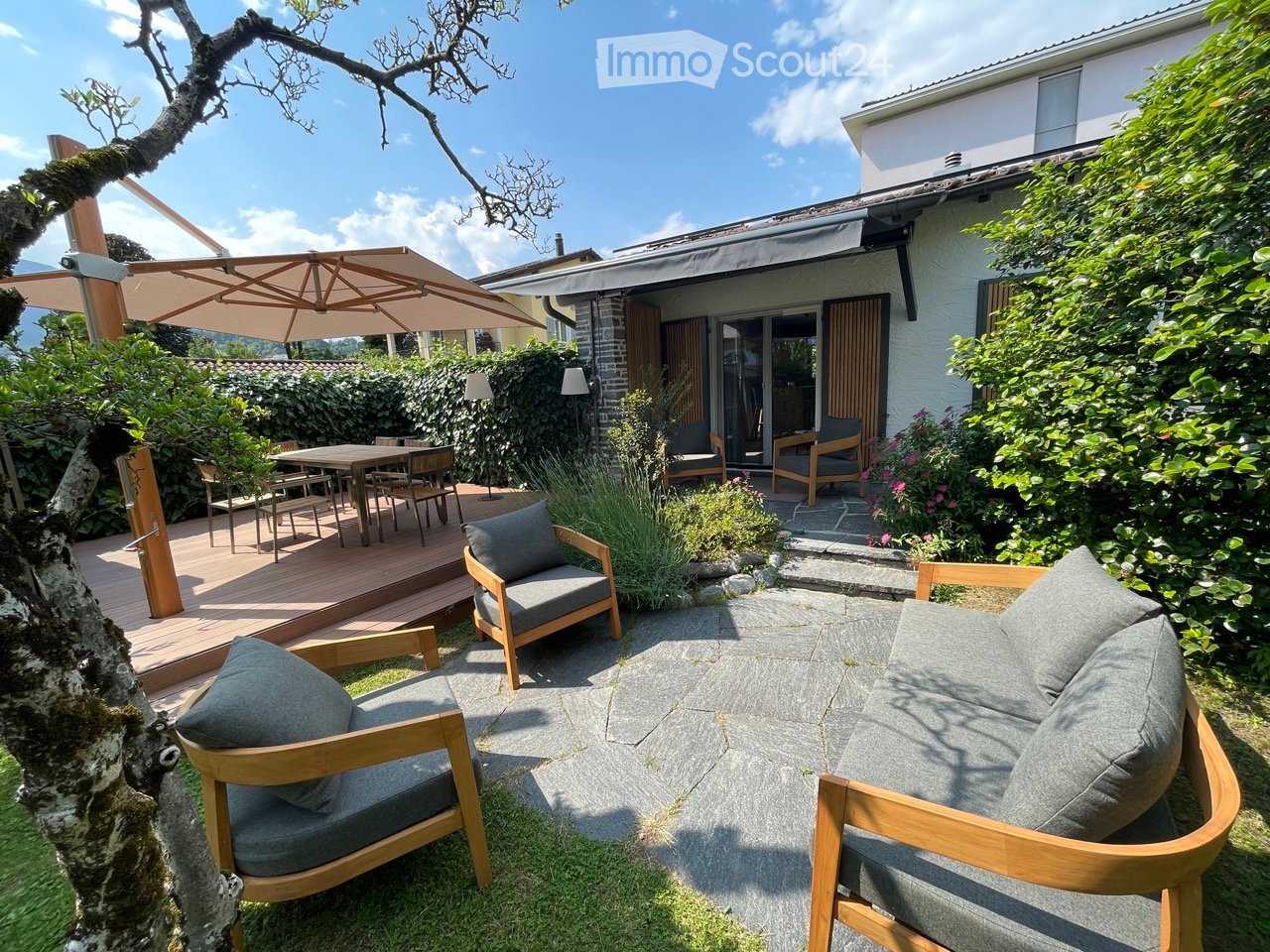 Outdoor seating with chairs and table, umbrella, stone patio, wooden deck, shrubs, small garden