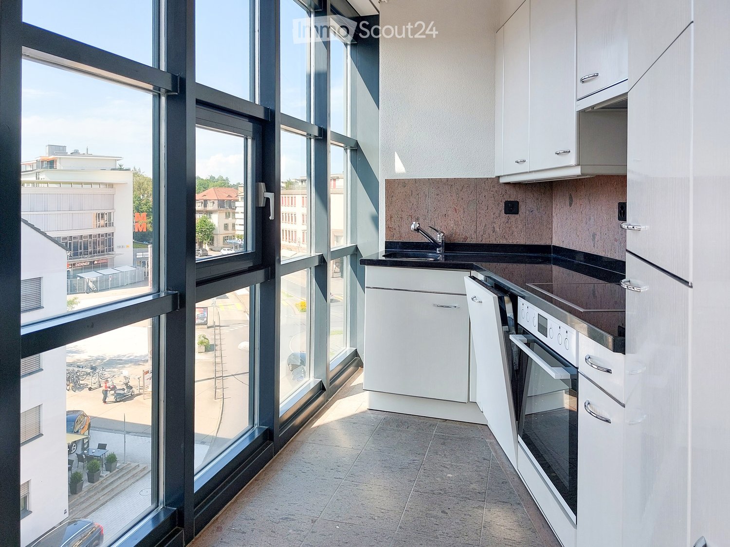 modern kitchen with large windows, white cabinets, black countertops, stainless steel sink, oven, refrigerator, and a view of the city