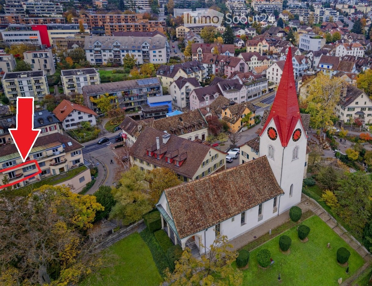 Church with red roof, surrounded by houses, trees, and grass, located in a city