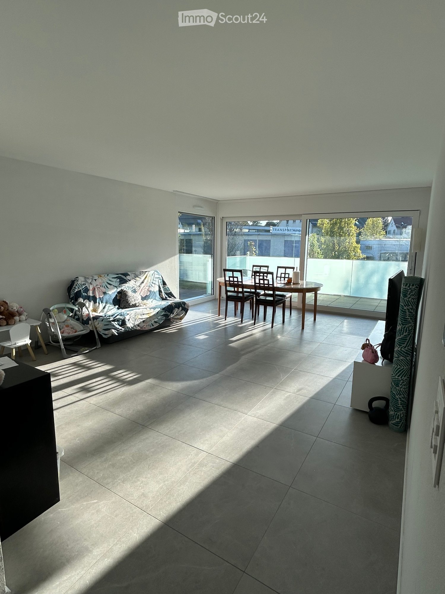 Furnished Room. Bright living room with tiled floor, large windows, sofa, dining table, chairs, baby chair, and small stool.
