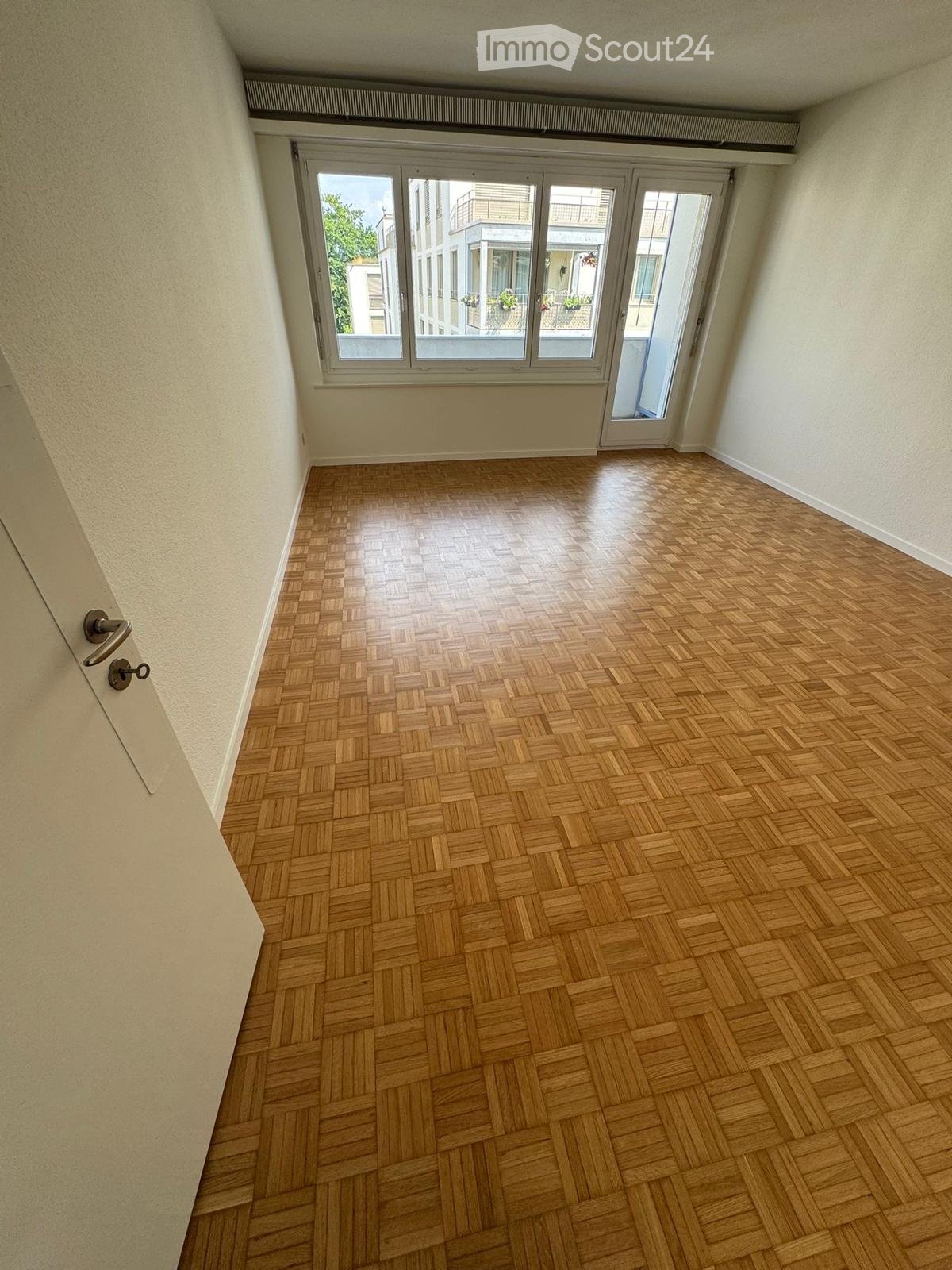large window with balcony, wooden parquet flooring, white walls
