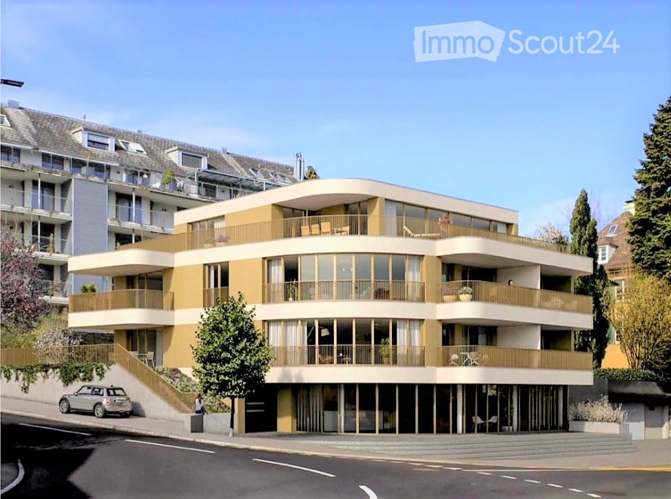 Building. Modern multi-story residential building with large windows, balconies, and a curved facade. The building features a combination of beige and yellow tones, with a staircase leading up to the entrance.