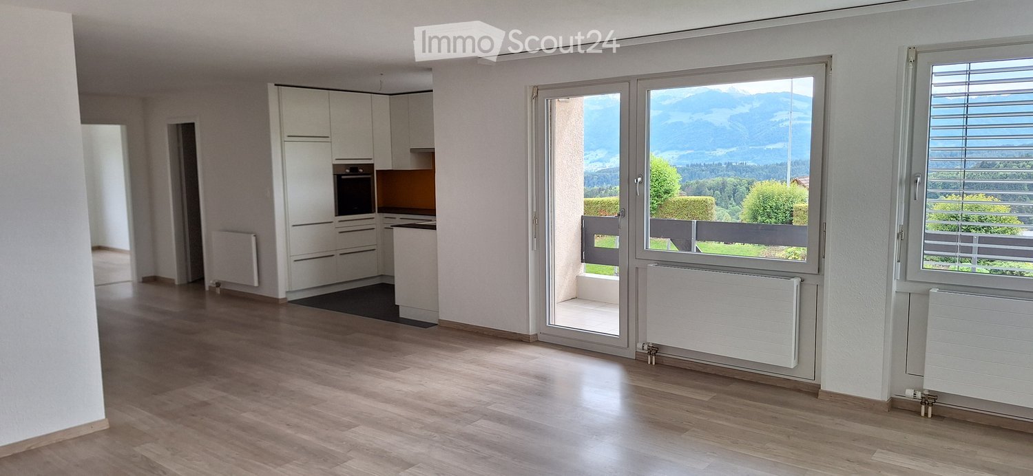 Furnished Room. Bright, open-plan living and dining area with wooden flooring, white cabinetry, and a view of the mountains through large windows and a sliding glass door.