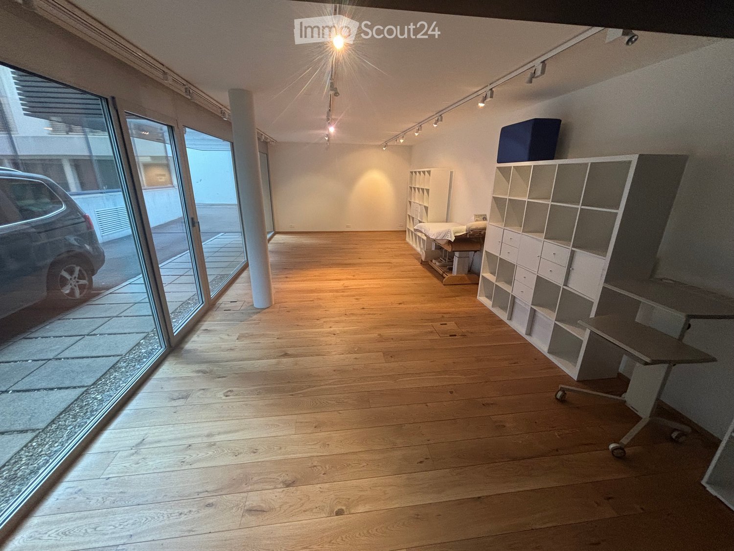 Bright, open room with wooden flooring, large glass sliding doors leading outside, white shelving units, a small table, and a stool.