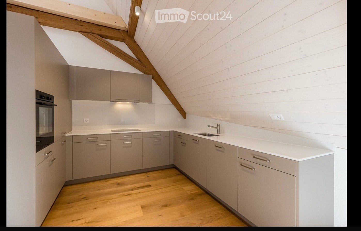 Modern kitchen with light grey cabinets, white countertops, wooden flooring, and exposed wooden beams on the ceiling.