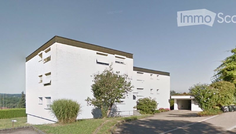 Modern white building with flat roof, multiple windows, and a small garage entrance.