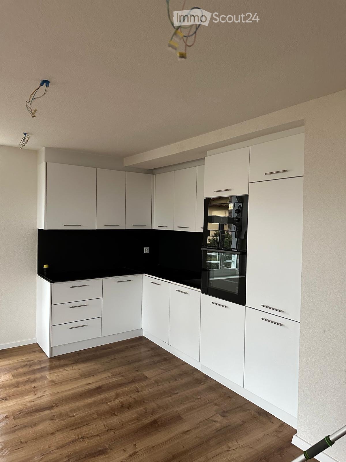 Modern kitchen with white cabinets, black countertop, and wooden flooring.