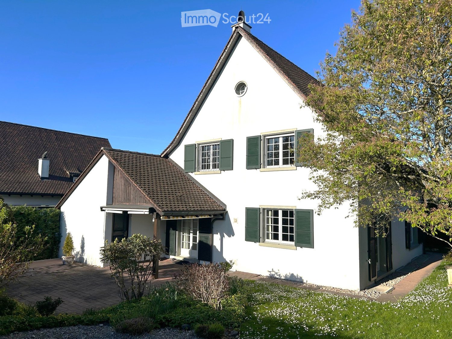 Detached house, white exterior, brown roof, green shutters, small garden, brick driveway, chimney