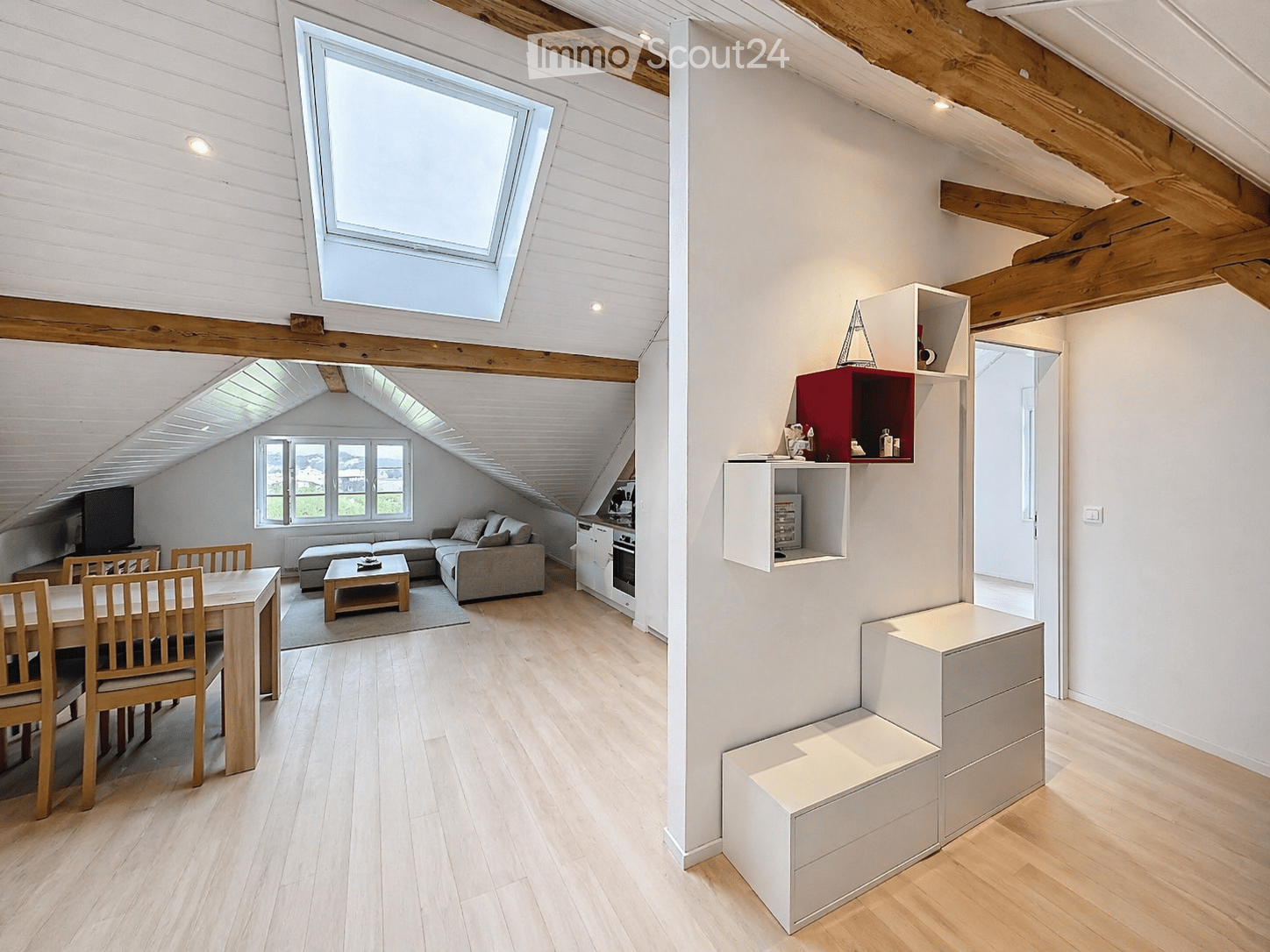 open-plan living room and dining area, wooden floor, white walls, skylight, dining table, chairs, couch, coffee table, TV, kitchen, shelves, storage drawers