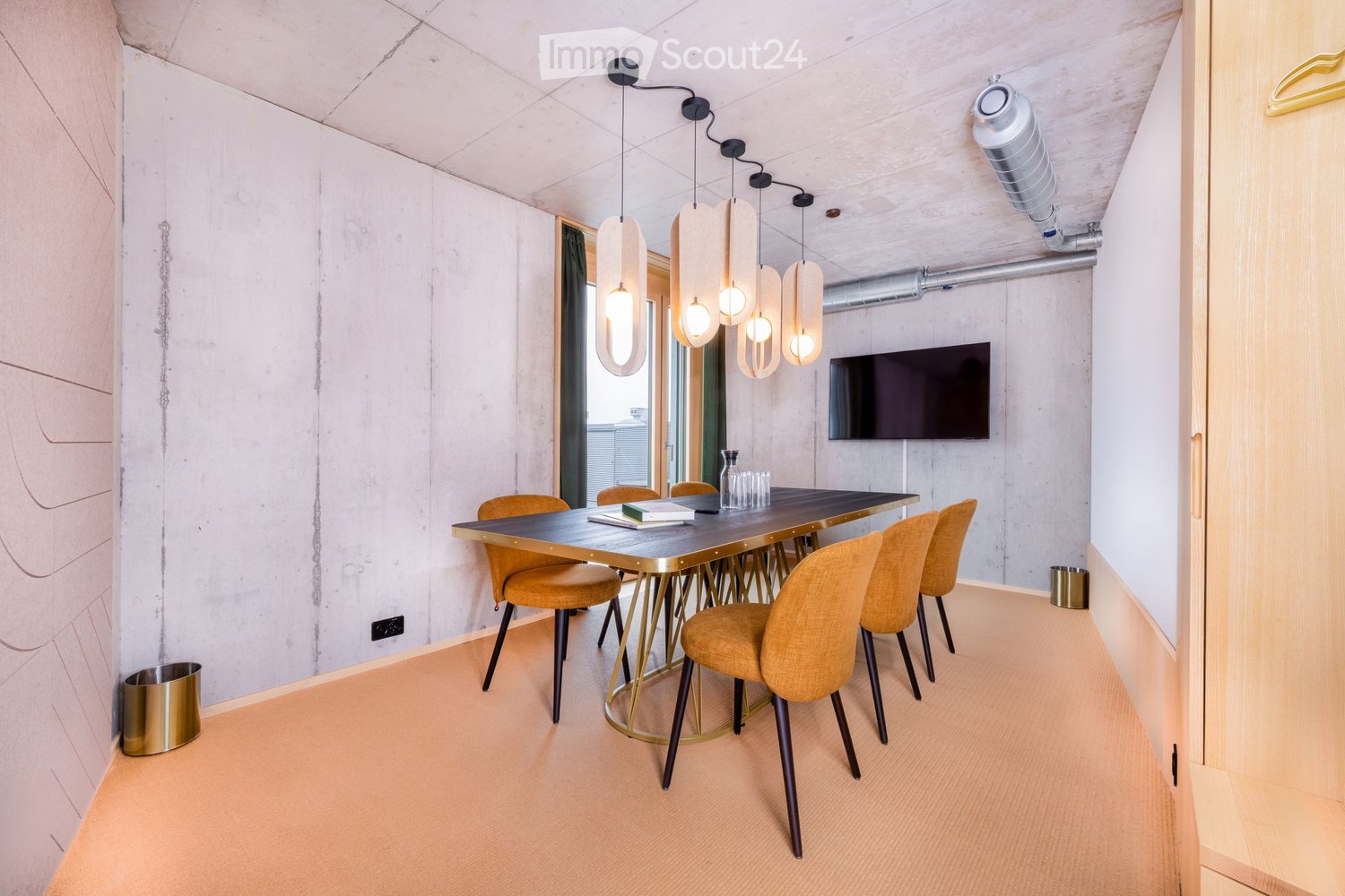 Modern dining area with a sleek black table, gold chairs, pendant lights, and a television mounted on the wall.