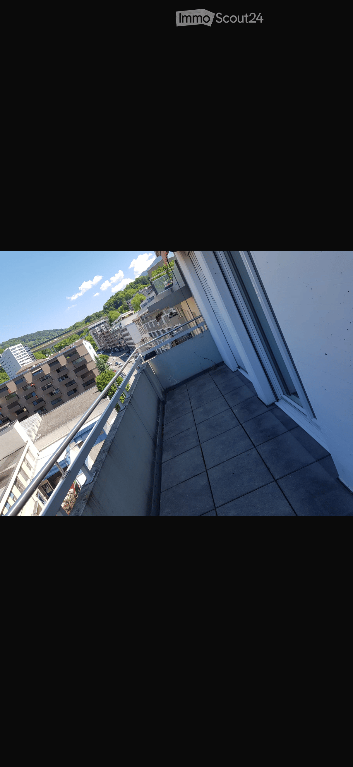 Balcony with tiled floor, metal railing, overlooking a cityscape with buildings and greenery.