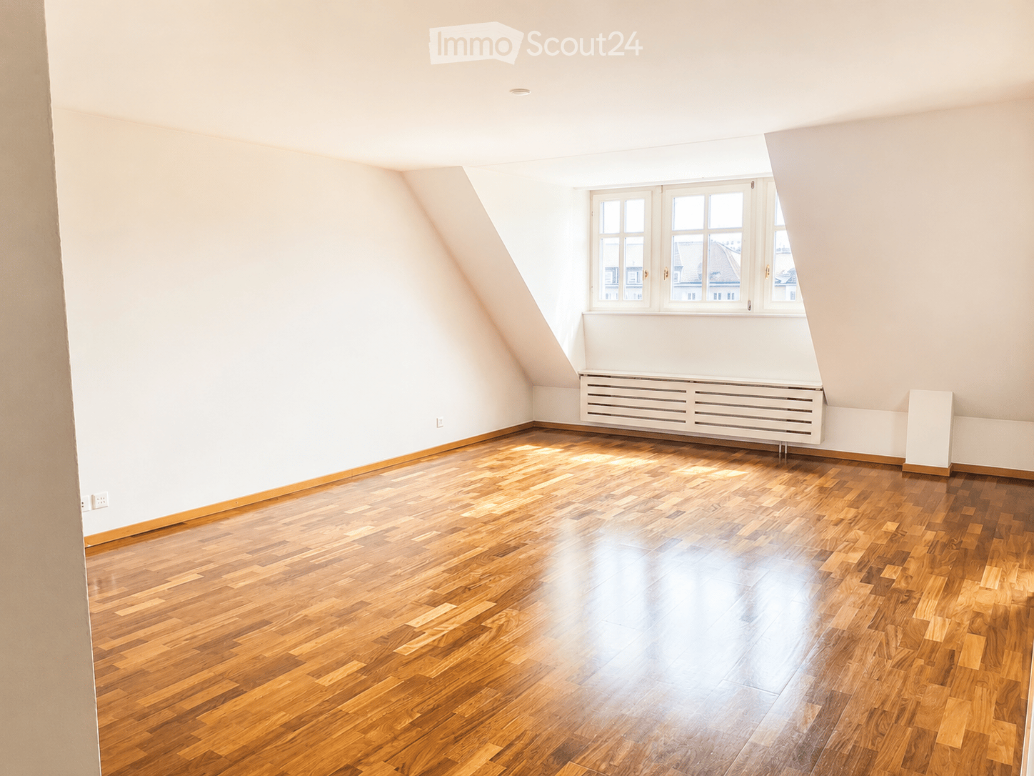 Empty attic room with wooden flooring, white walls, and large windows allowing natural light to enter.