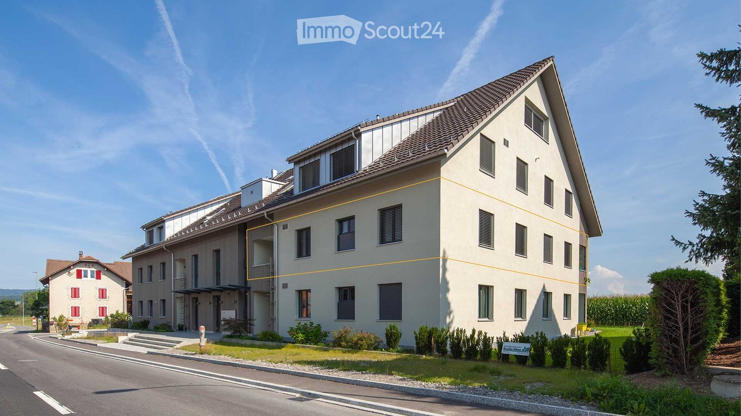 Modern multi-story residential building with a sloped roof, multiple windows, and a small balcony area on the upper level.