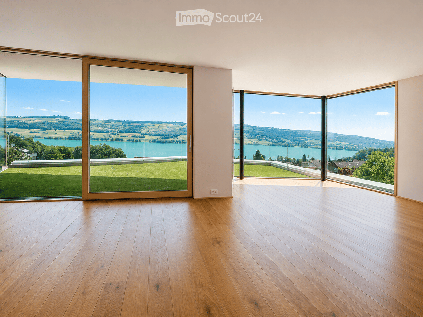 Empty room with wooden flooring, large glass sliding doors, and scenic view of a lake and landscape.