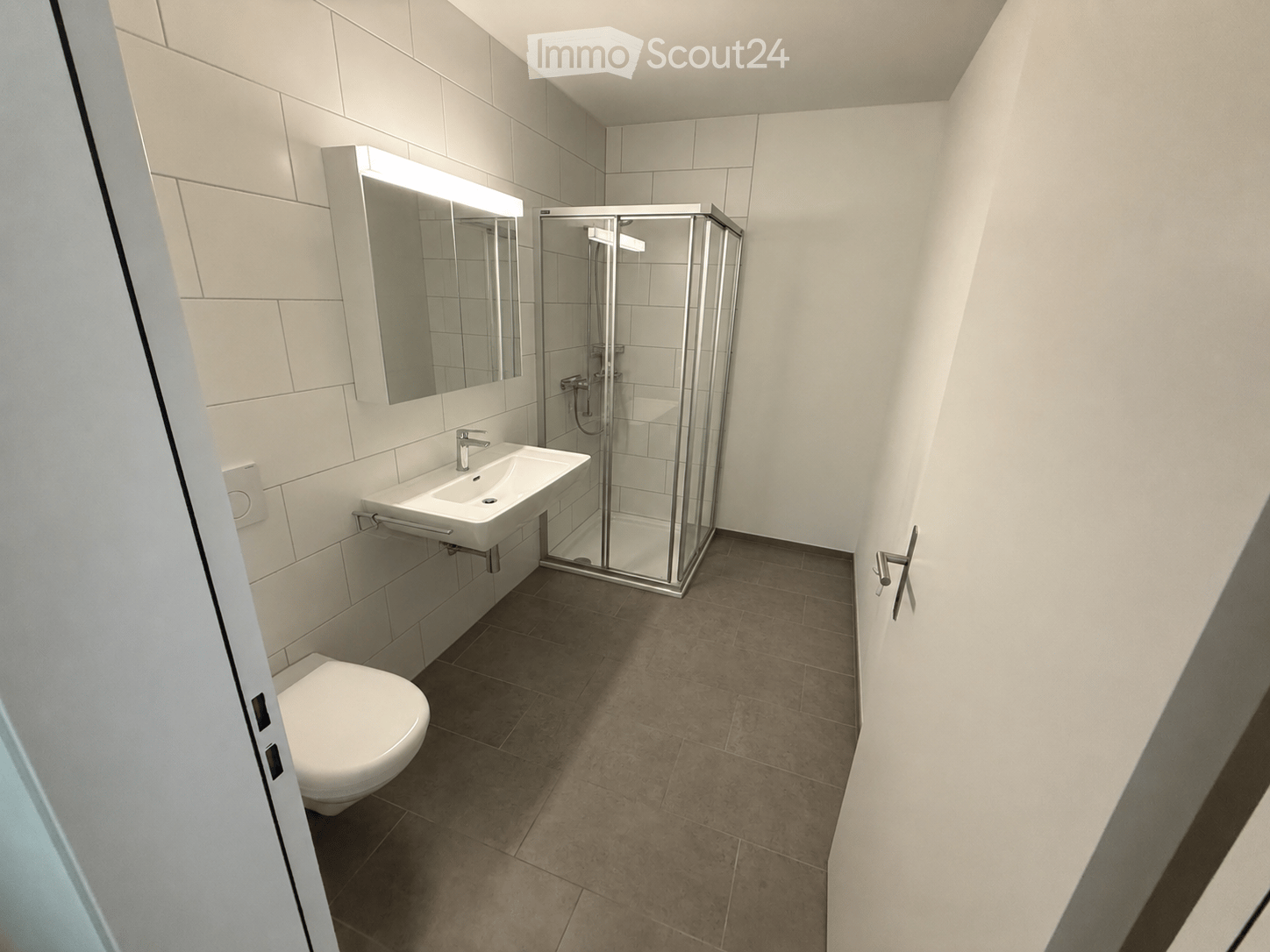 Modern bathroom with white tiles, a toilet, a sink with a mirror, and a glass-enclosed shower stall.
