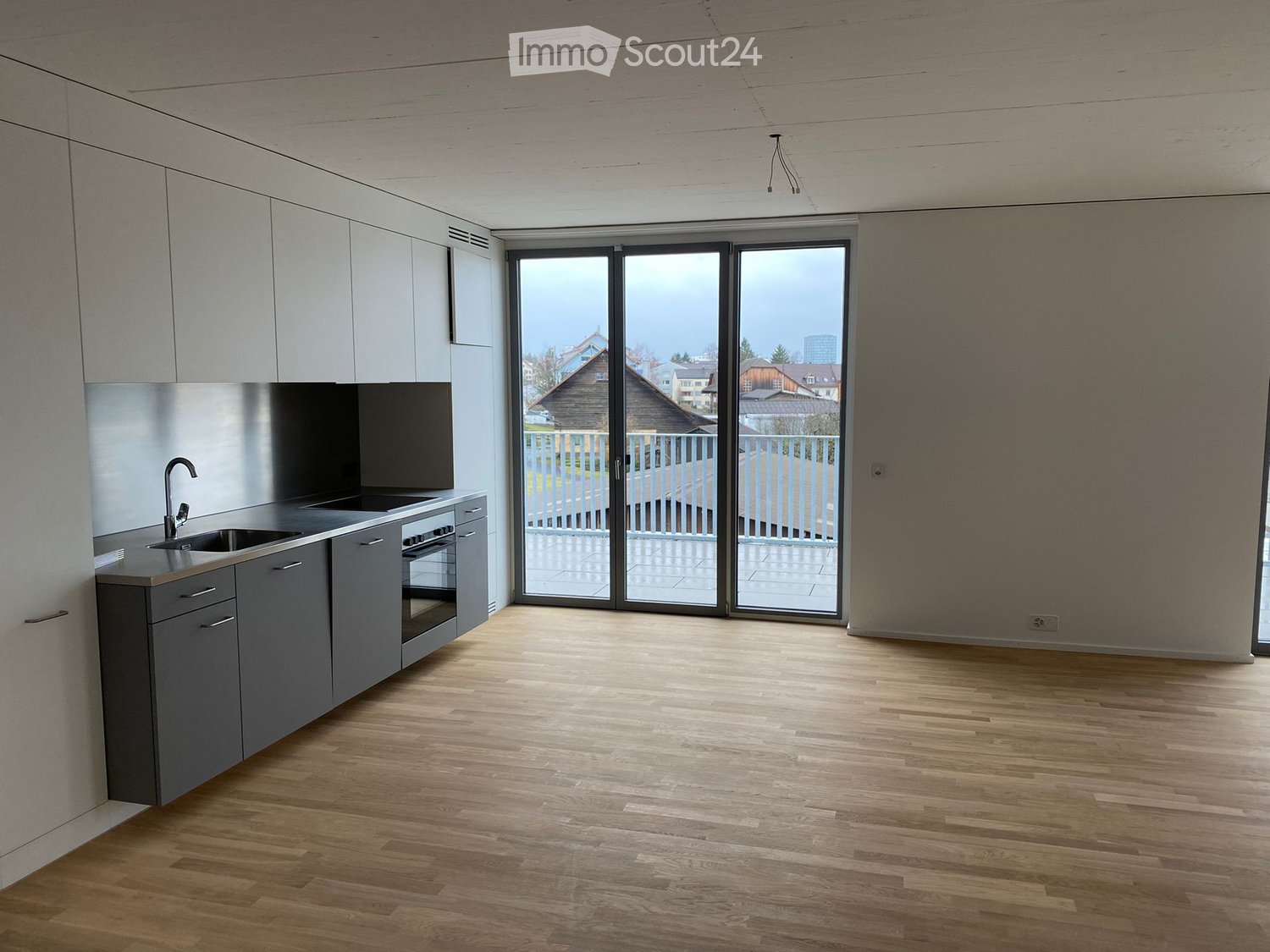 Modern kitchen with grey cabinets, wooden flooring, and large sliding glass doors leading to a balcony.