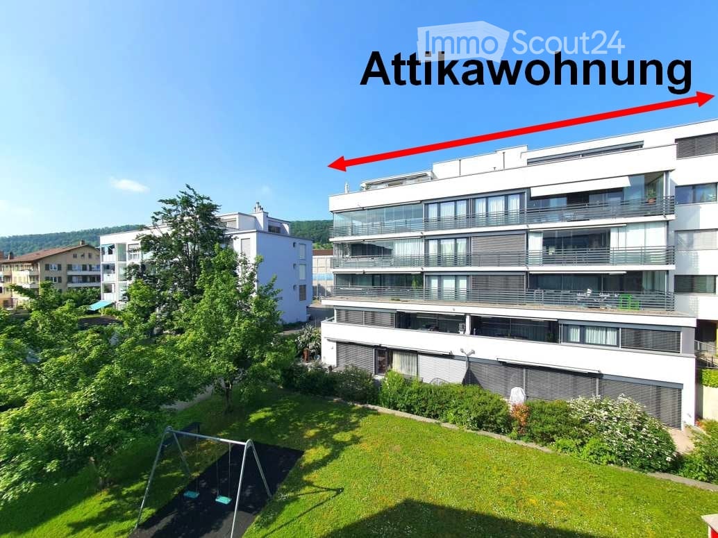 Modern multi-story residential building with large windows and balconies, surrounded by greenery and a playground.