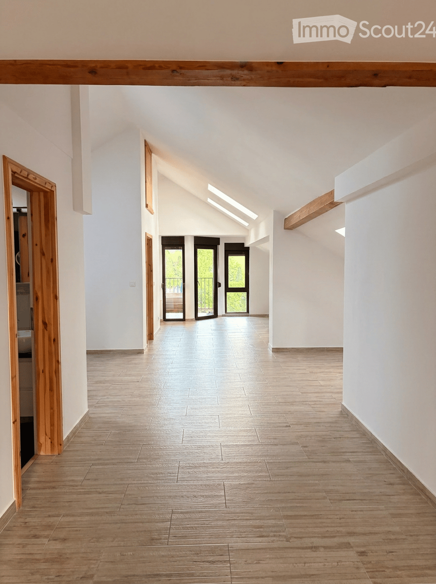 Bright, open hallway with wooden flooring, white walls, and large glass doors leading to an outdoor area.