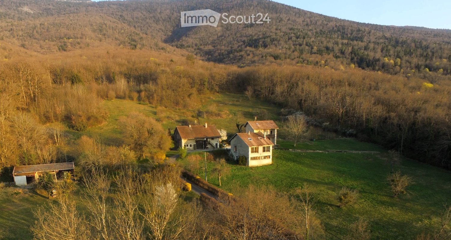 Aerial view of a rural property with three houses, surrounded by forested hills and open fields.