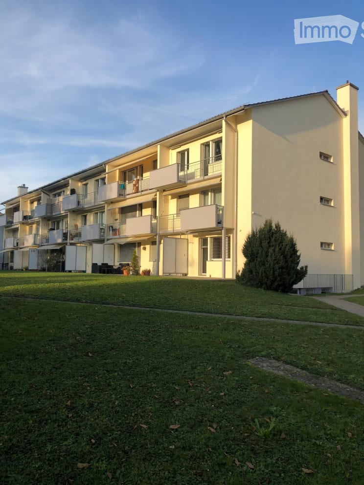 Multi-story residential building with multiple balconies and a well-maintained lawn in front.