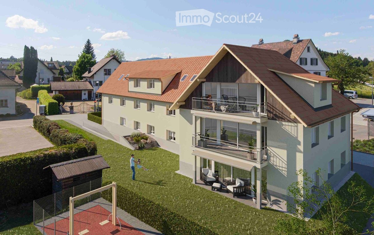 A two-story house with a red-tiled roof, white walls, and multiple balconies. The house is surrounded by a well-maintained lawn, garden, and a small playground area.