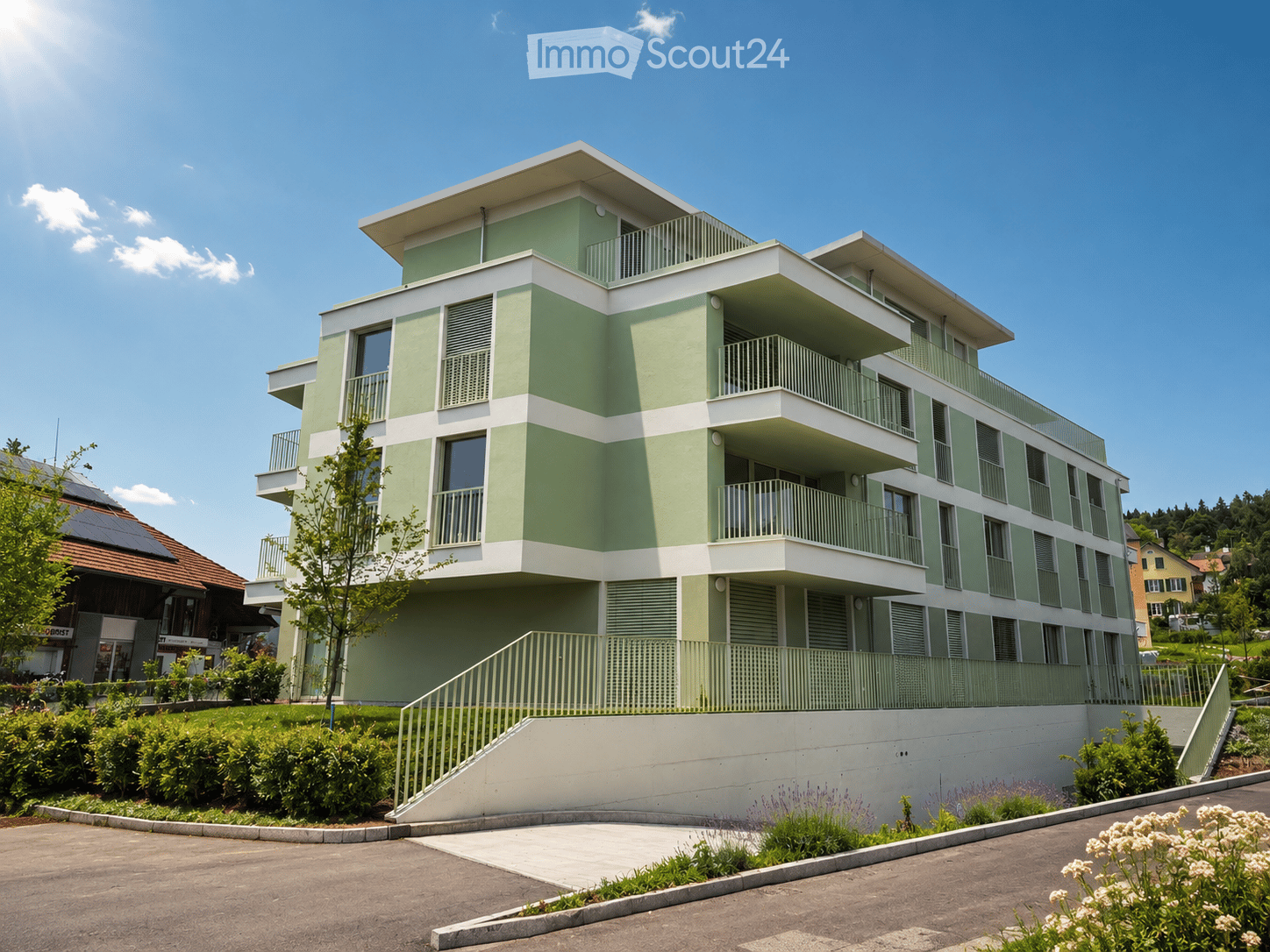 Modern three-story residential building with green and white exterior, multiple balconies, and a raised ground floor entrance.