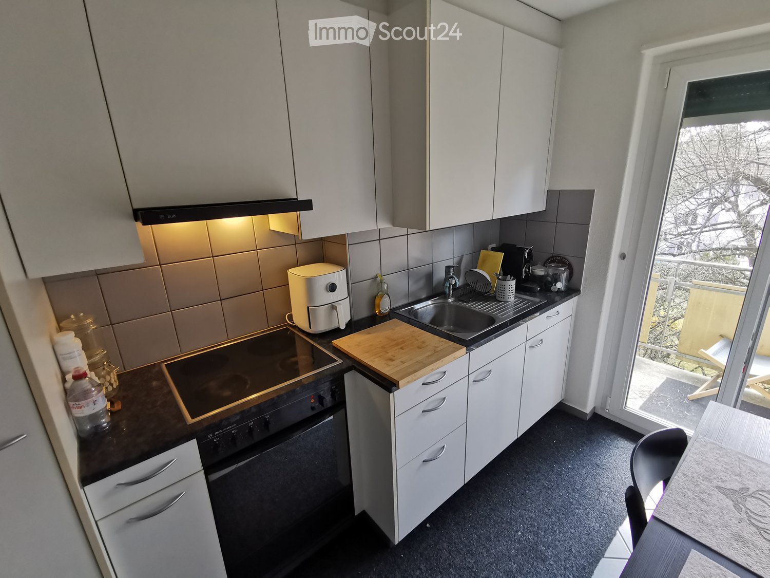 Modern kitchen with white cabinets, dark countertops, built-in oven, sink, and various appliances.
