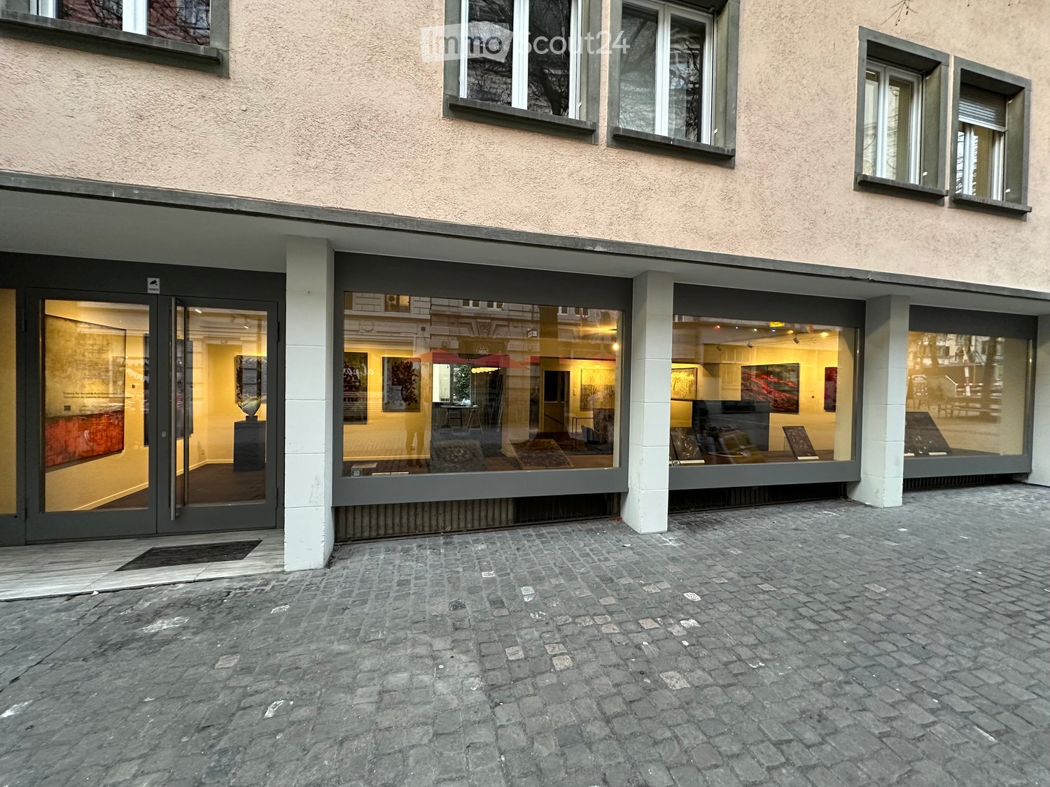 Exterior view of a multi-story building with large windows and glass doors leading to an art gallery or exhibition space inside.
