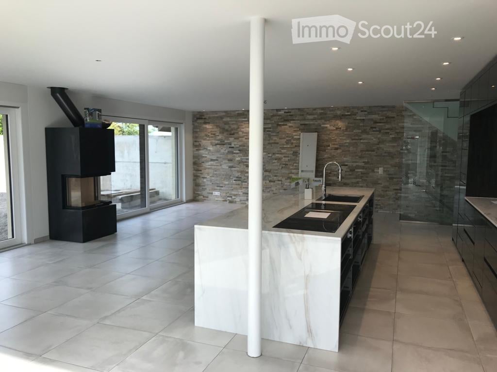 Modern kitchen with a large island, built-in sink, sleek faucet, and a prominent fireplace on the left side.