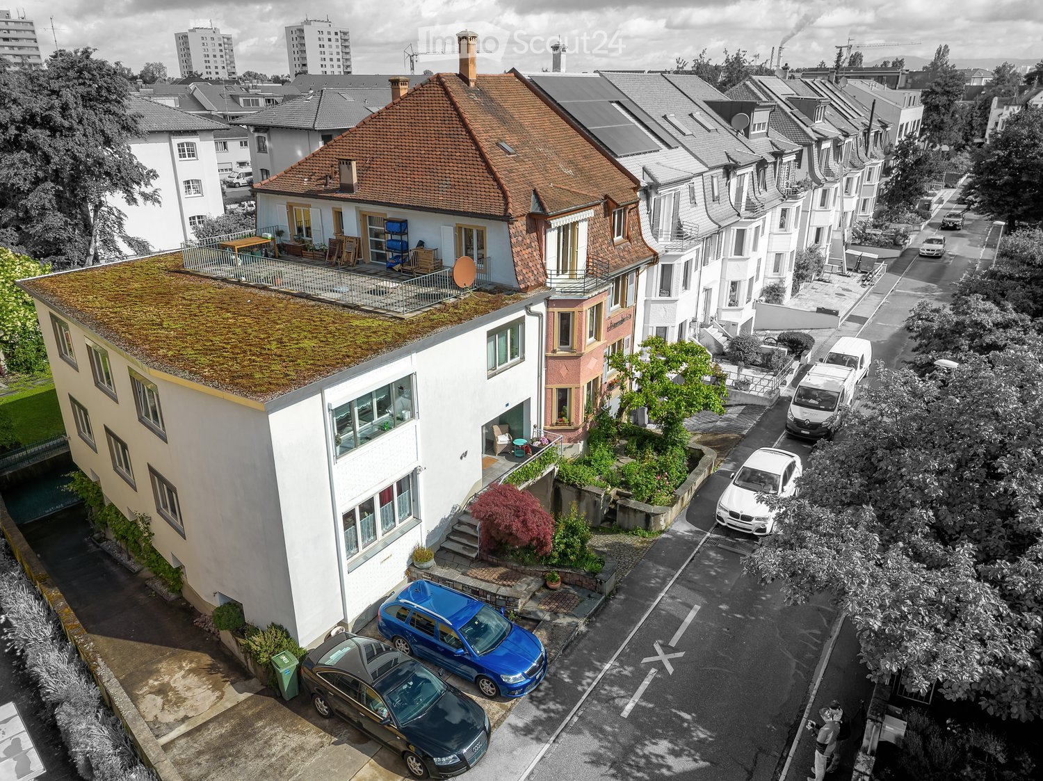 Aerial view of a residential area with multiple houses, parked cars, and greenery.