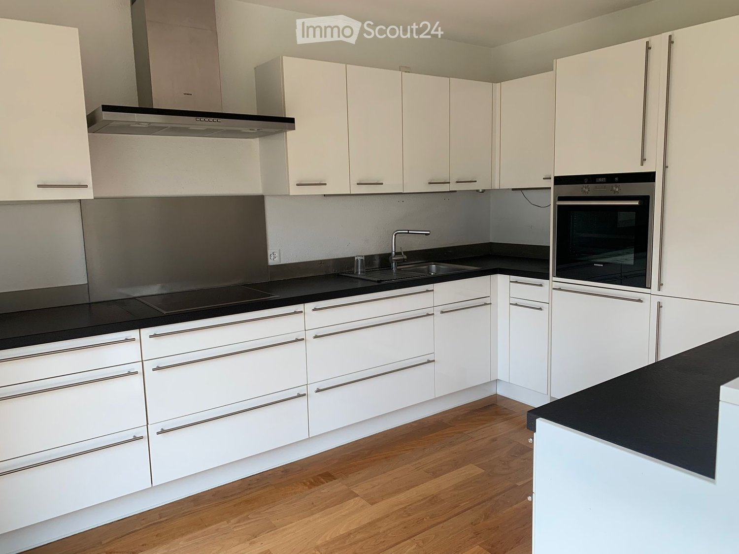 Modern kitchen with white cabinets, black countertops, and stainless steel appliances including a sink, faucet, and oven.