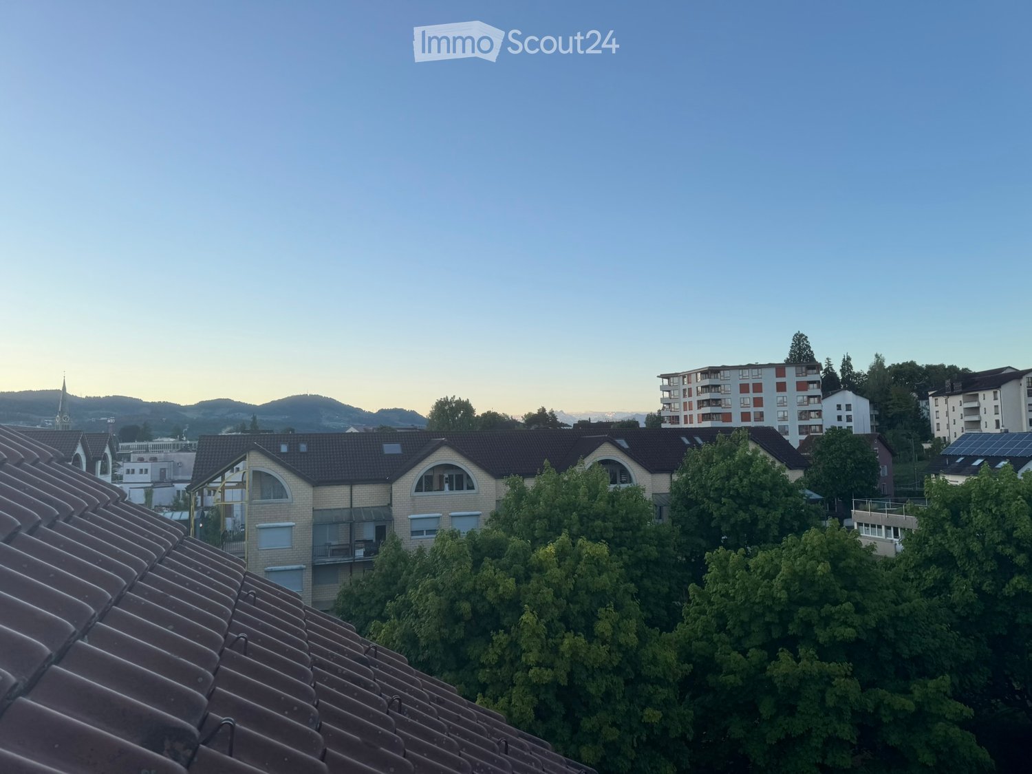 Building. Residential buildings with tiled roofs, balconies, and surrounding greenery, viewed from a rooftop perspective during twilight.