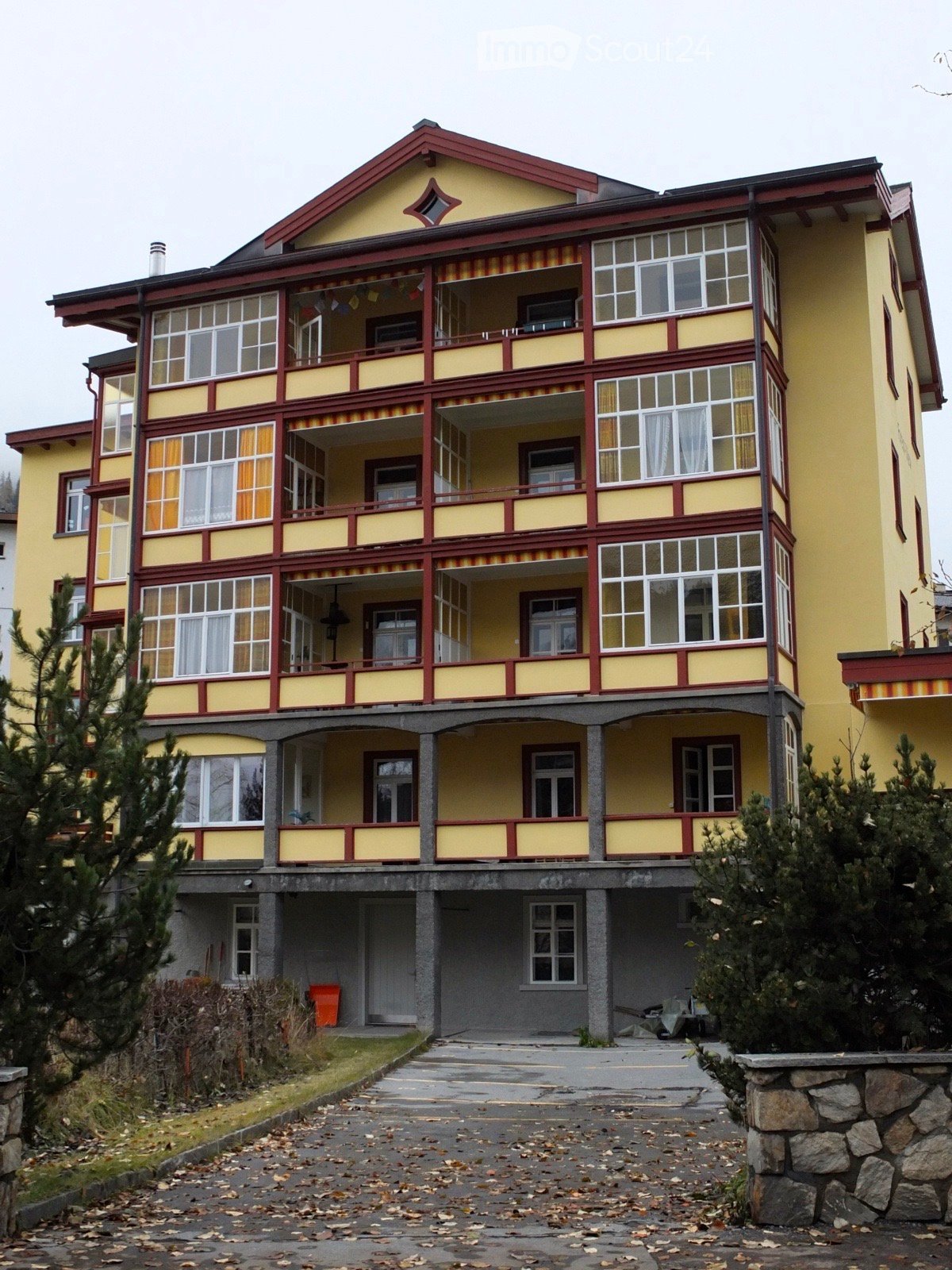 A large, multi-story building with yellow walls and red trim, featuring multiple balconies and large windows. The structure has a classic architectural style with decorative railings and a prominent roofline.