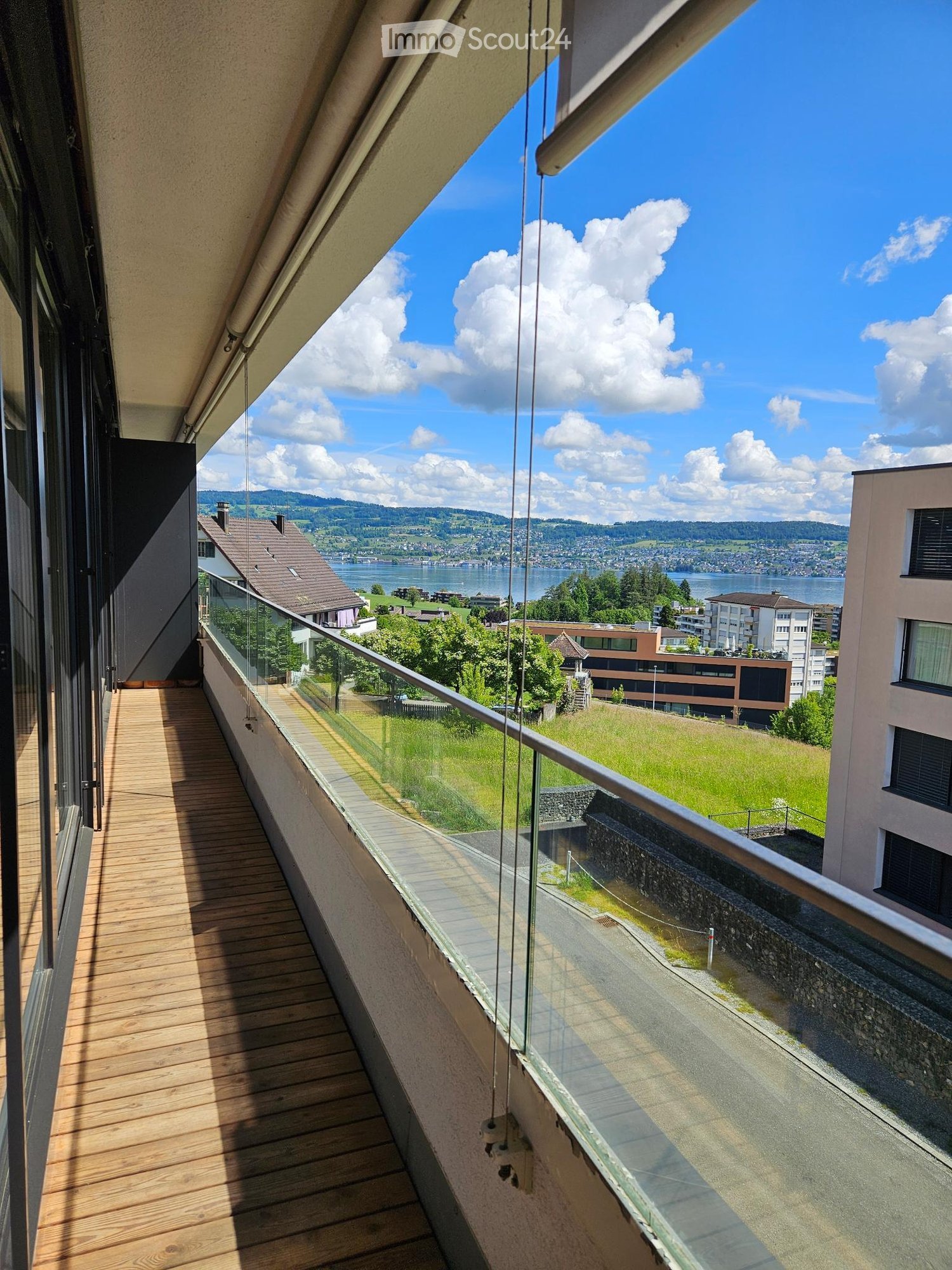 Balcony with wooden decking, glass railing, overlooking a scenic lake and distant mountains.