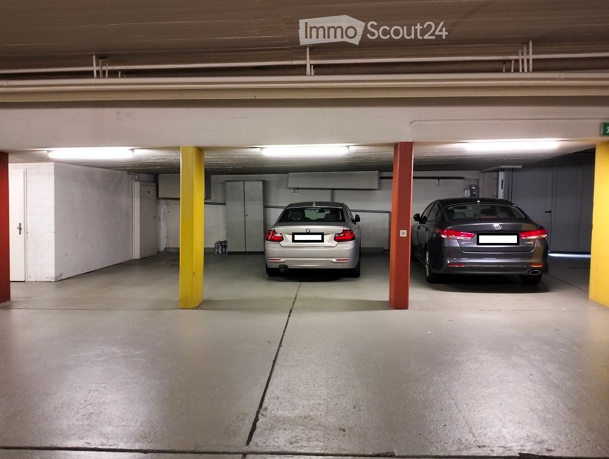 Underground parking area with two parked cars, concrete floor, yellow and red support pillars, and fluorescent lighting.