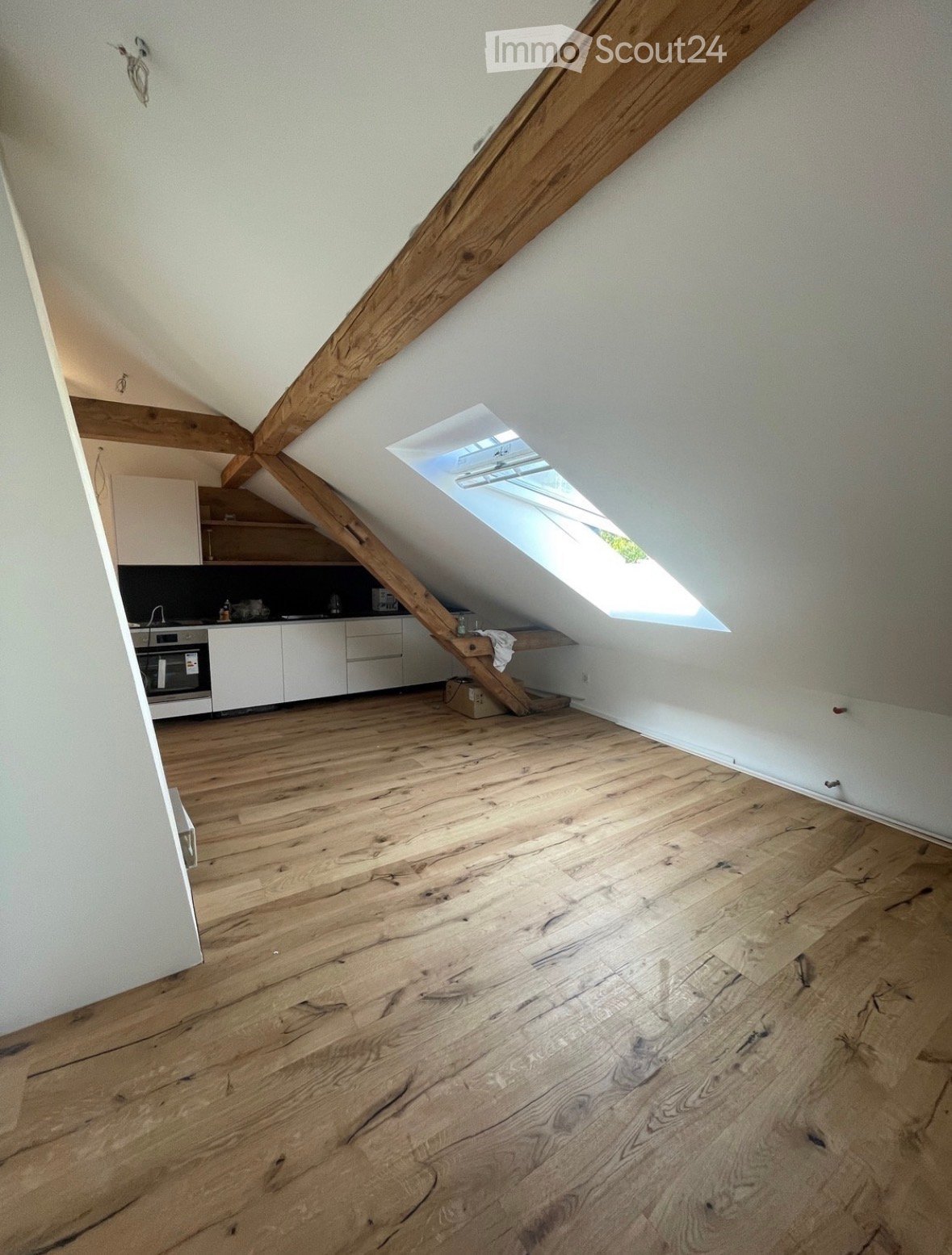 An attic space with wooden floors, exposed wooden beams, and a skylight window allowing natural light to enter. The room is empty, with no furniture or decorations.
