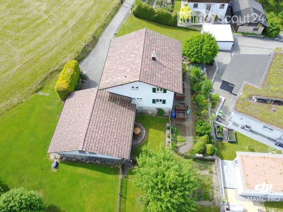 Aerial view of a two-story house with a brown tiled roof, surrounded by a well-maintained lawn, garden, and neighboring houses.