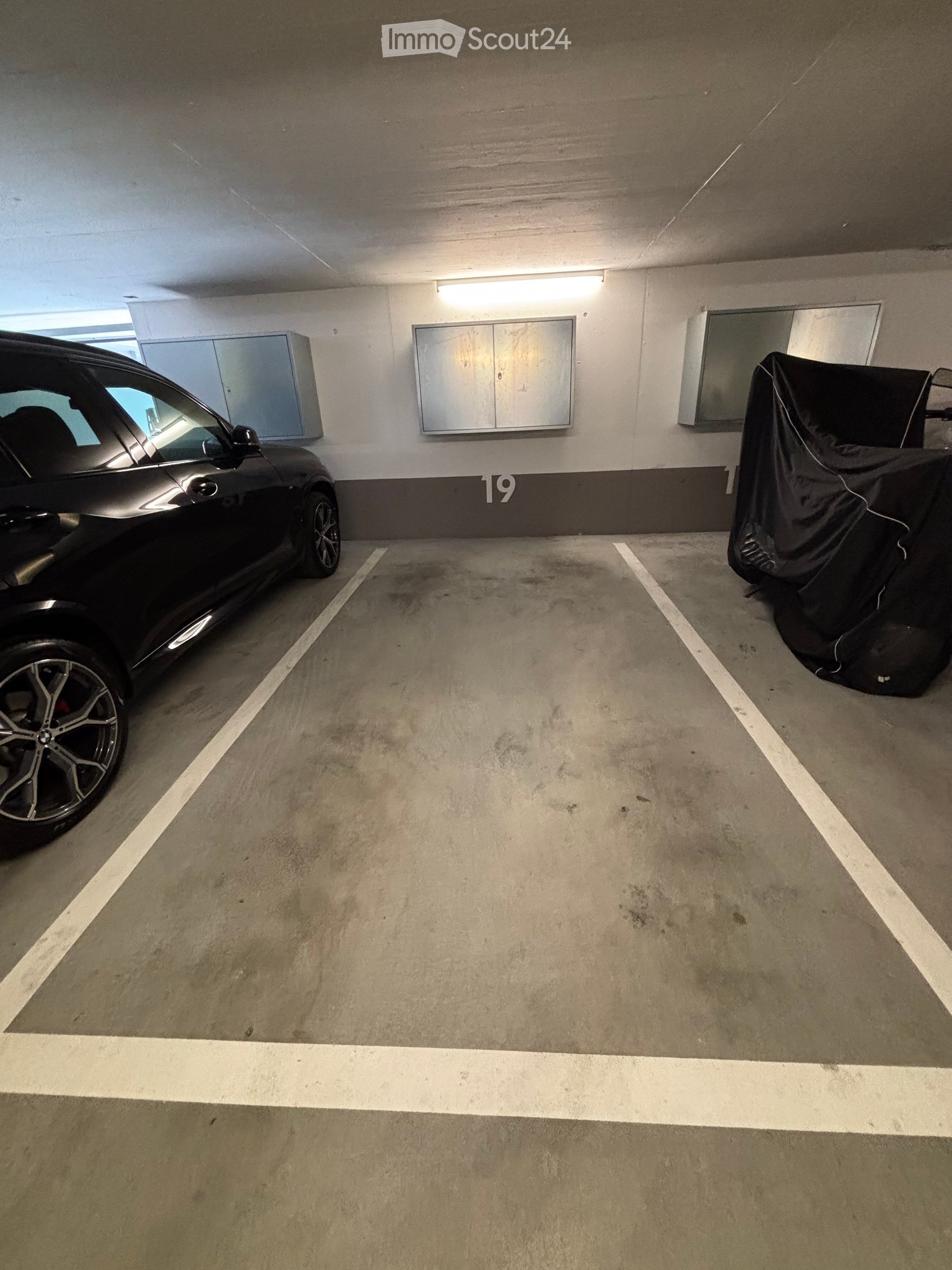Underground parking space with one car parked and a covered vehicle on the right side.