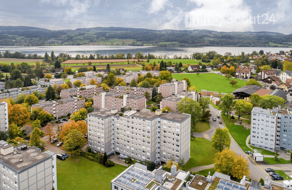 Aerial view of a residential area with multiple apartment buildings, green spaces, and a lake in the background.