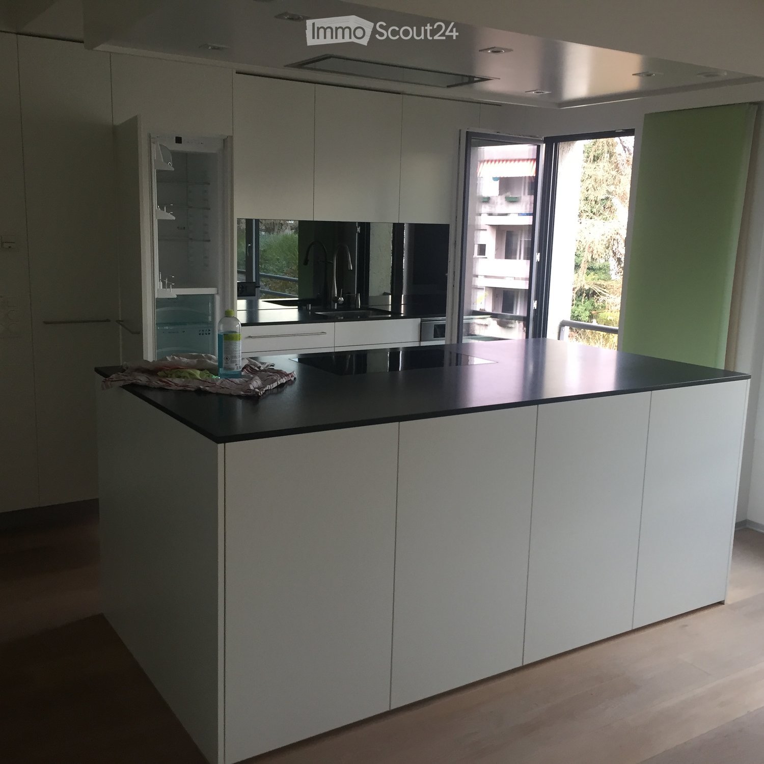Modern kitchen with white cabinets, black countertop, and a sink area. A bottle is placed on the counter, and a cleaning cloth is visible.