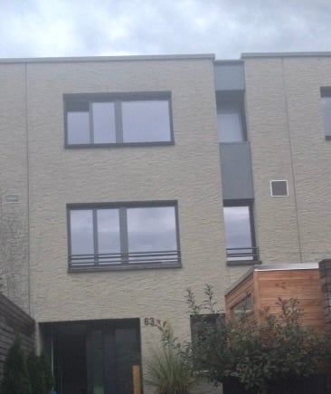 Modern two-story building with large windows, grey facade, and a small balcony on the right side.