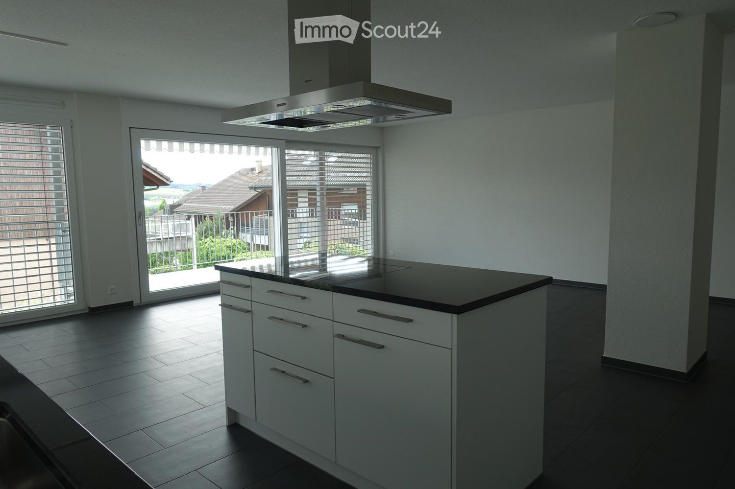 Modern kitchen with white cabinets, a central island, and a range hood. Large windows and sliding doors lead to a balcony.