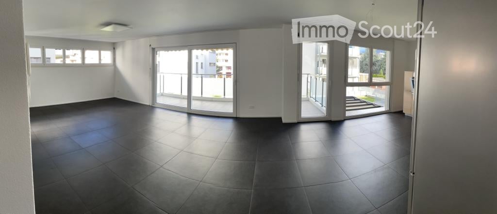 Empty room with dark tiled floor, white walls, large sliding glass doors leading to a balcony, and several windows allowing natural light.