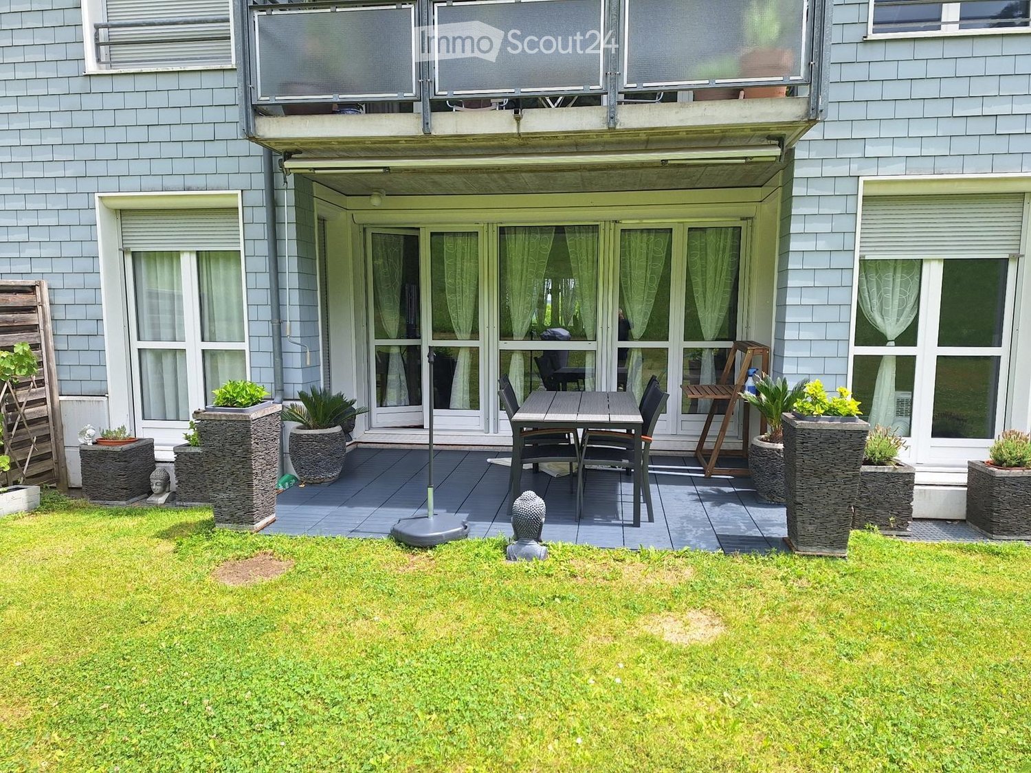 Garden with a well-maintained lawn, a patio area with a table and chairs, potted plants, and a small wooden structure.